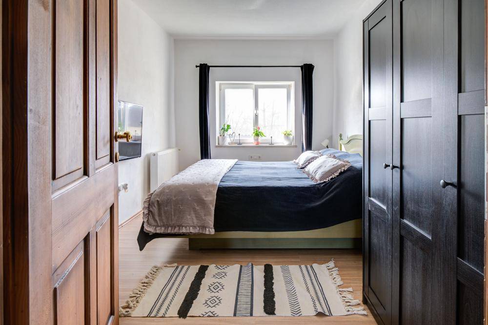 Schlafzimmer mit Doppelbett, Holzboden und dunklen Schränken, gut beleuchtet durch ein Fenster.