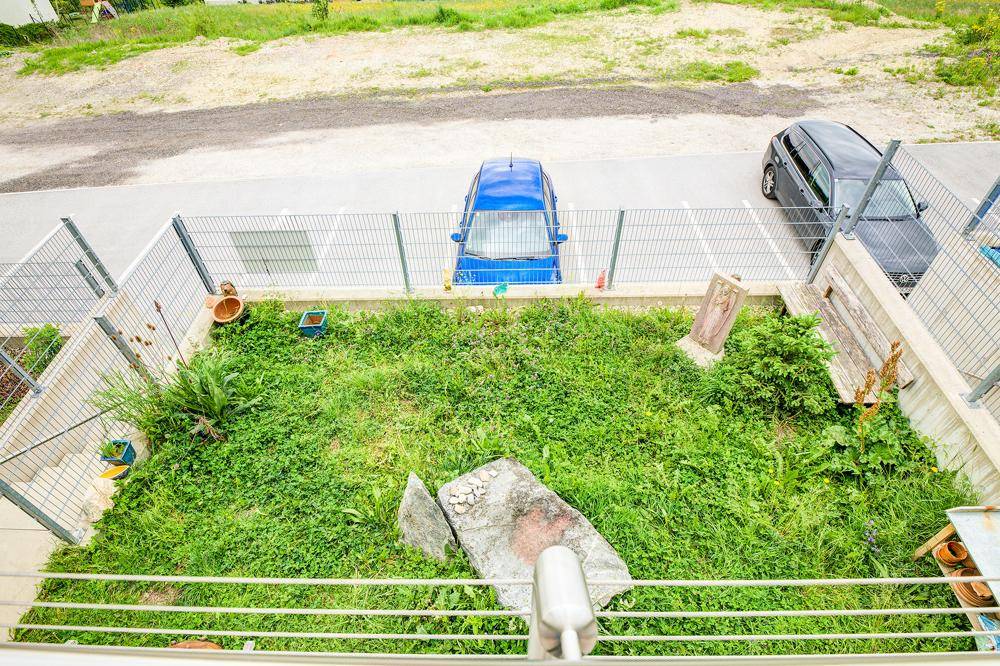 Blick von oben auf einen kleinen, eingezäunten Gartenbereich mit Rasen und angrenzender Straße.