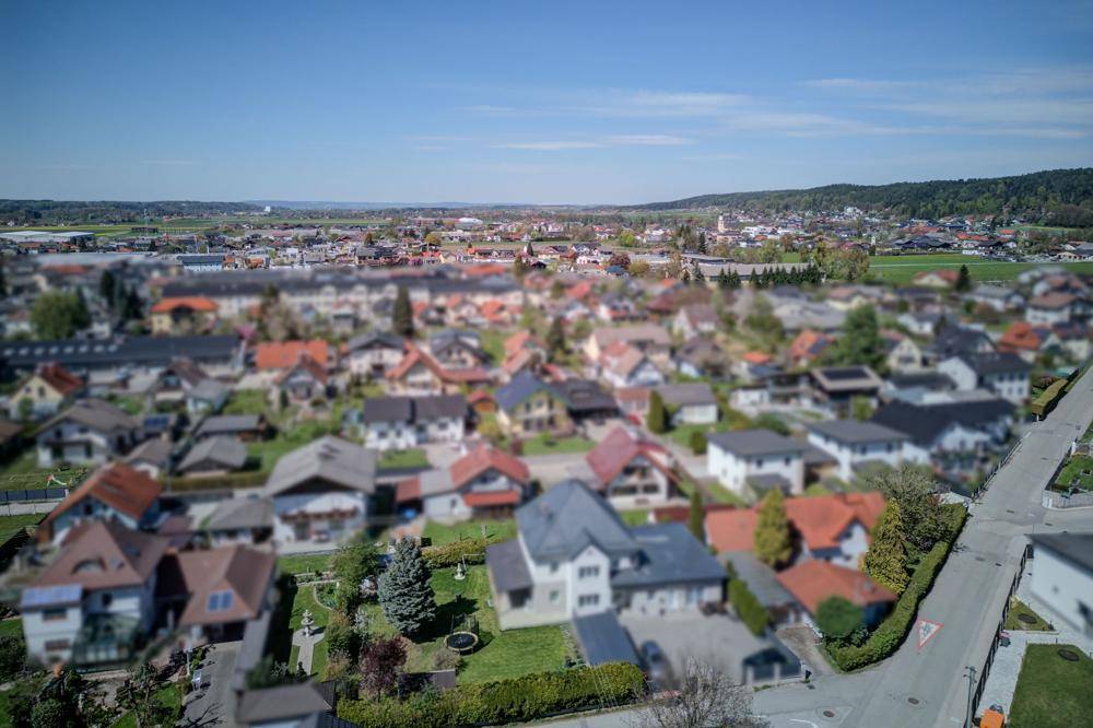 Weitläufige Wohnsiedlung mit Einfamilienhäusern und grünen Gärten unter blauem Himmel.