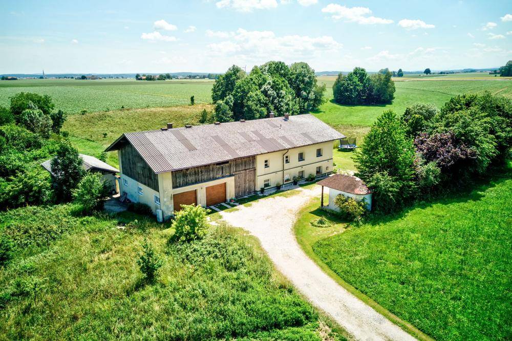 Luftaufnahme des Landhauses mit Zufahrt und angrenzenden Feldern unter strahlendem Himmel.