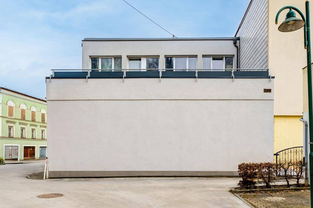 Seitenansicht des Gebäudes mit einer langen, geschlossenen Fassade und Fenstern im oberen Bereich.