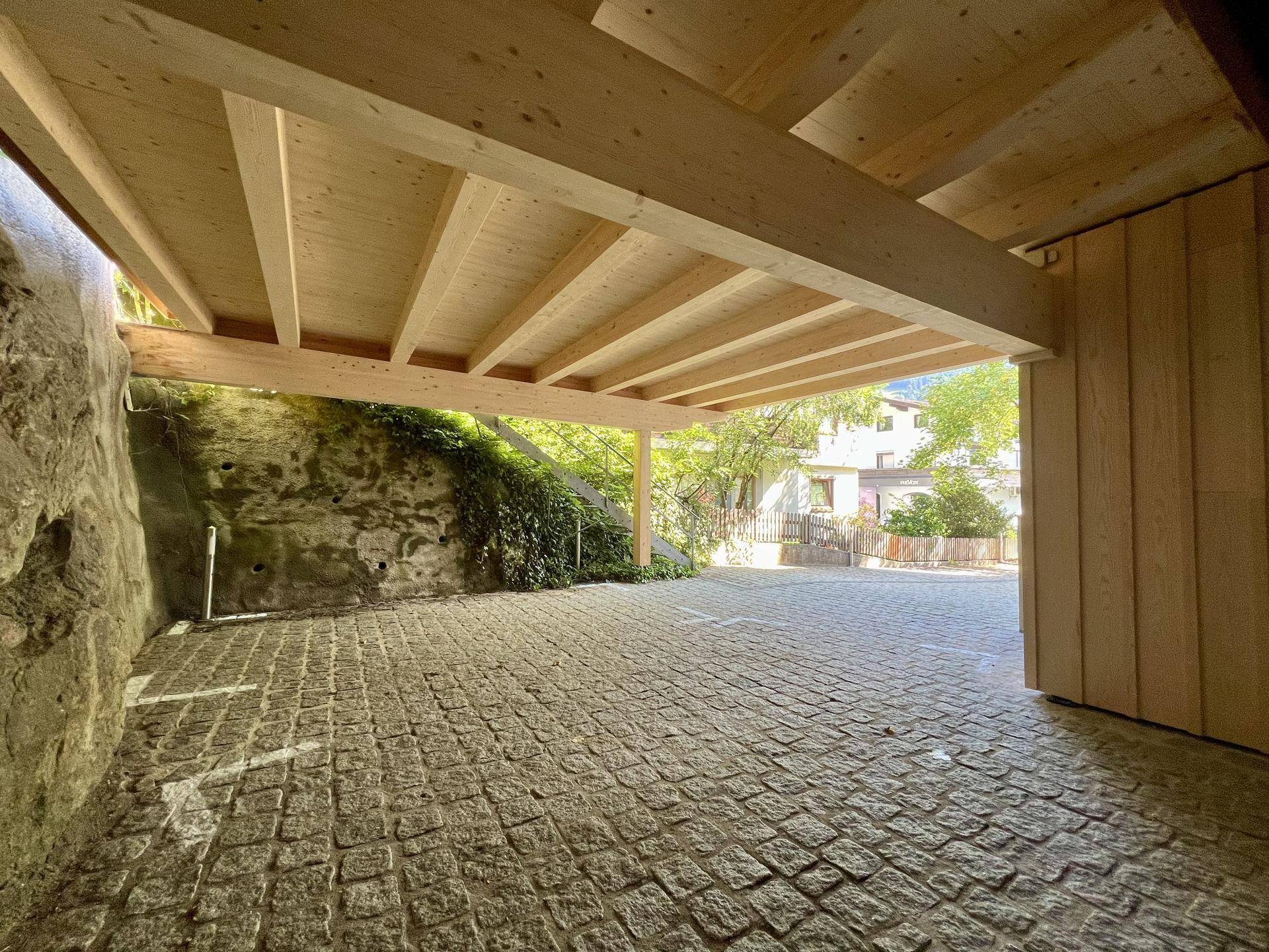Überdachter Parkplatz mit Kopfsteinpflaster und sichtbarer Holzkonstruktion des Carports.