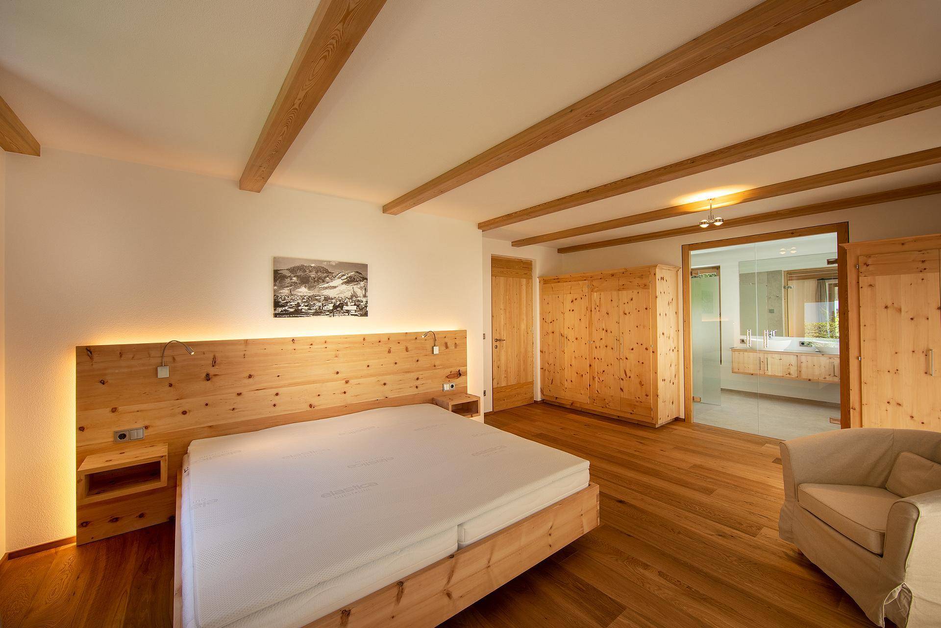 Gemütliches Schlafzimmer mit Holzbalken, Einbauschränken und direktem Zugang zum modernen Bad.