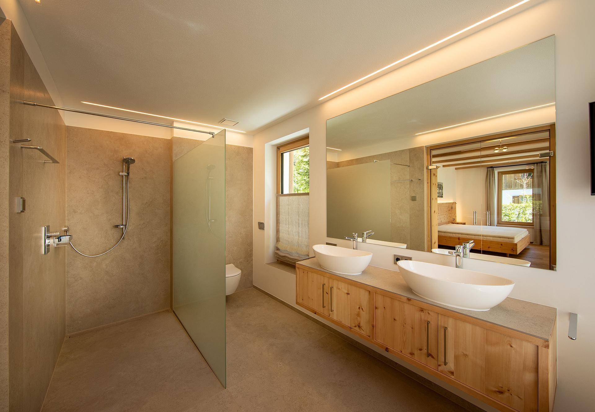 Modernes Badezimmer mit begehbarer Dusche, Doppelwaschbecken und großem beleuchtetem Spiegel.