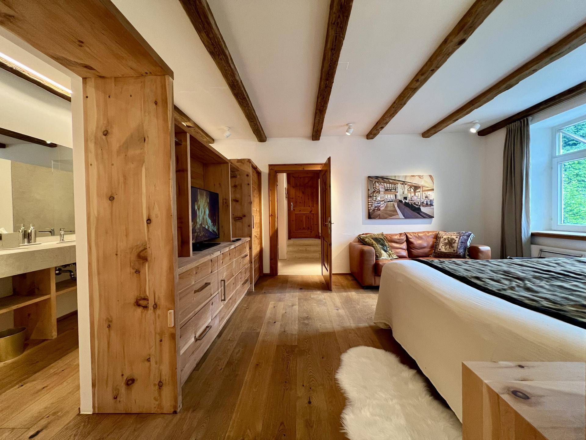 Schlafzimmer mit Holzbalken, Parkettboden und integriertem Badezimmerbereich mit Doppelwaschbecken.
