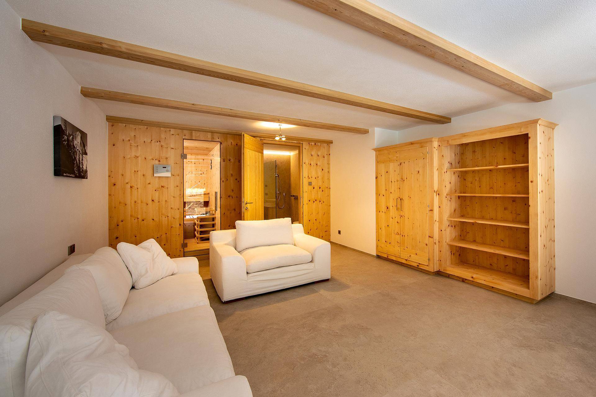 Entspannungsbereich mit Sofa, Holzregal und integrierter Sauna für Wellnessmomente.