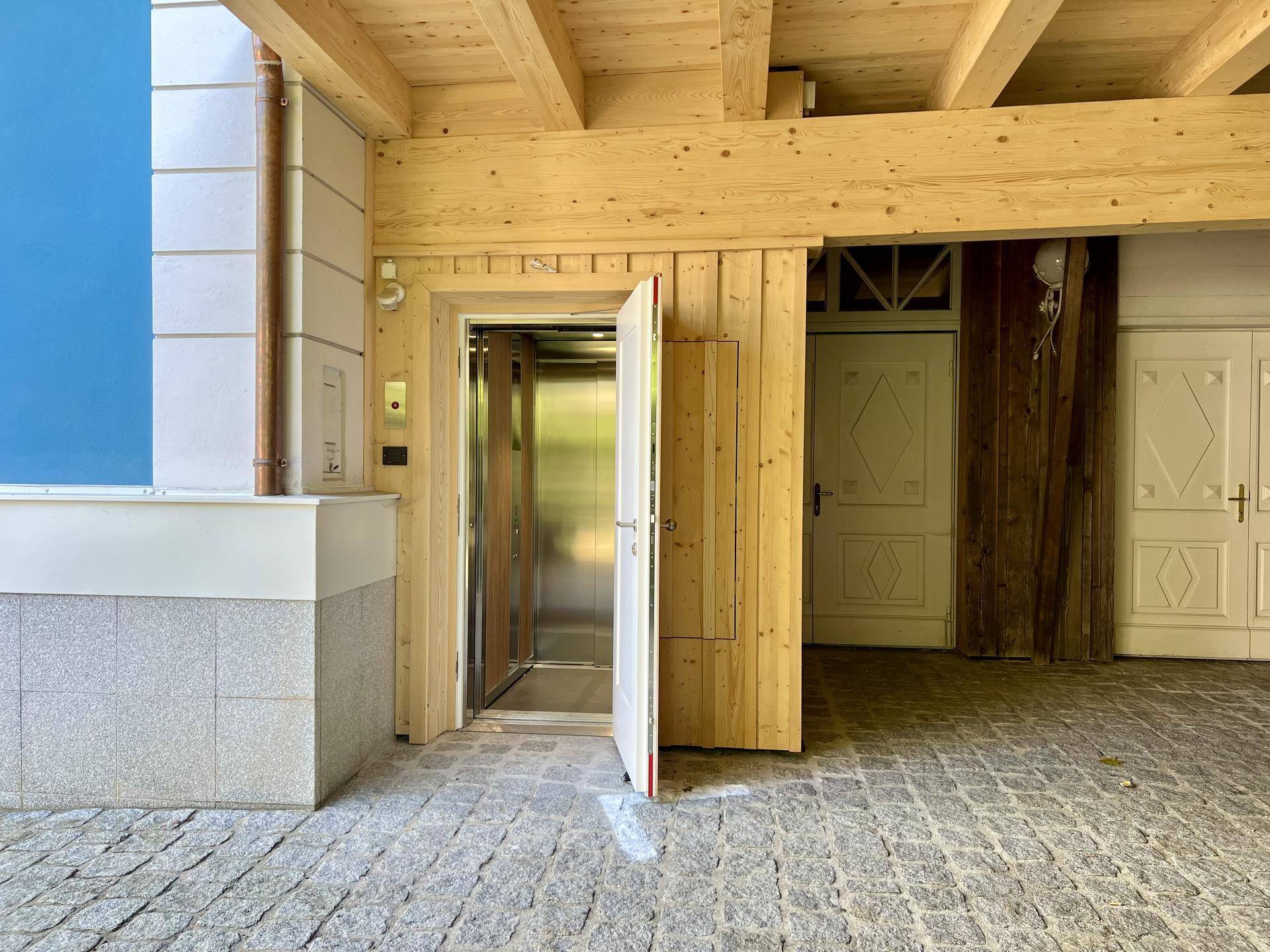 Eingangsbereich mit Aufzug und gepflastertem Boden, der Zugang zum Gebäude bietet.