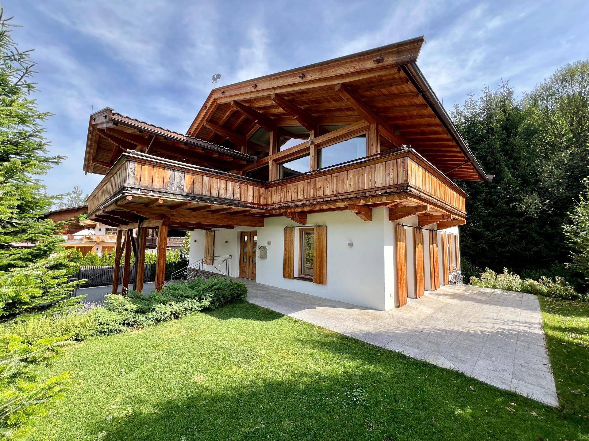 Attraktives Holzhaus im alpinen Stil mit großem Garten und gepflegter Außenanlage unter blauem Himmel.