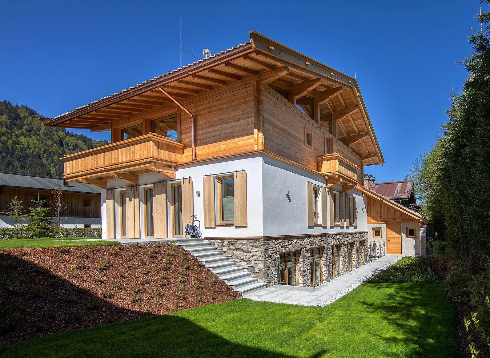 Modernes Holzhaus mit weißer Fassade, Steinsockel und großzügiger Grünfläche am Hang.