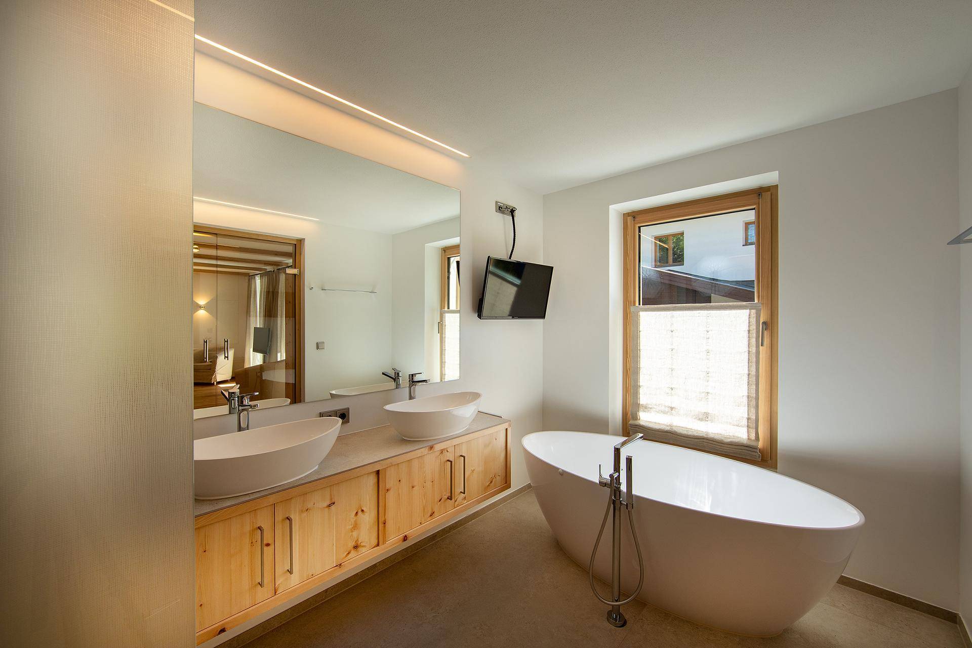 Elegantes Badezimmer mit freistehender Badewanne, Doppelwaschbecken und großem Spiegel.