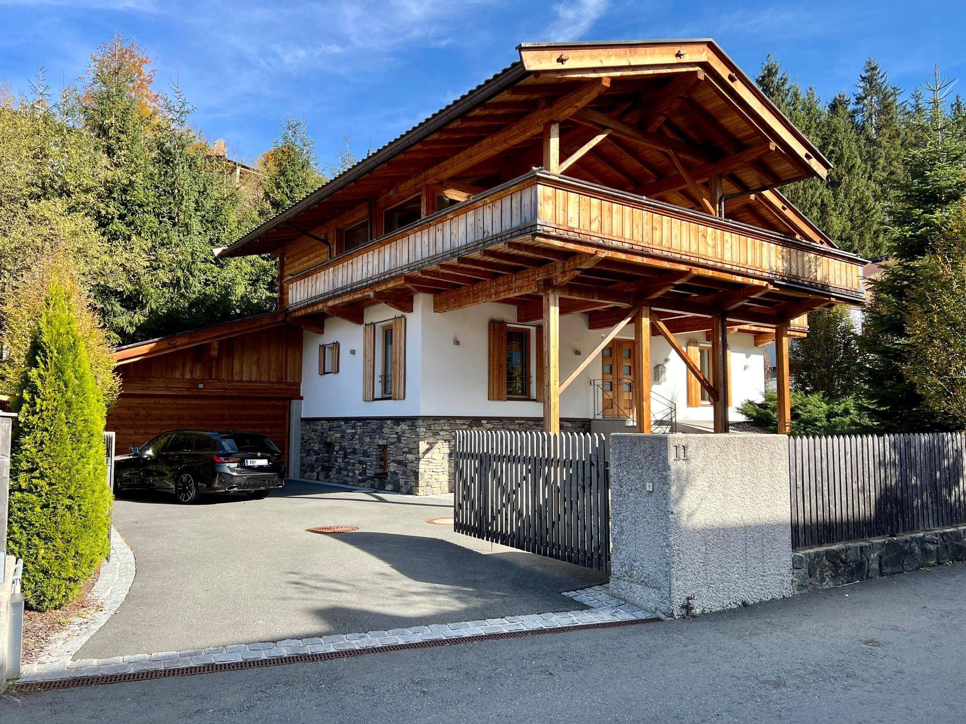 Charmantes Holzhaus mit Steinsockel, Balkonen und gepflegter Zufahrt in bergiger Umgebung.