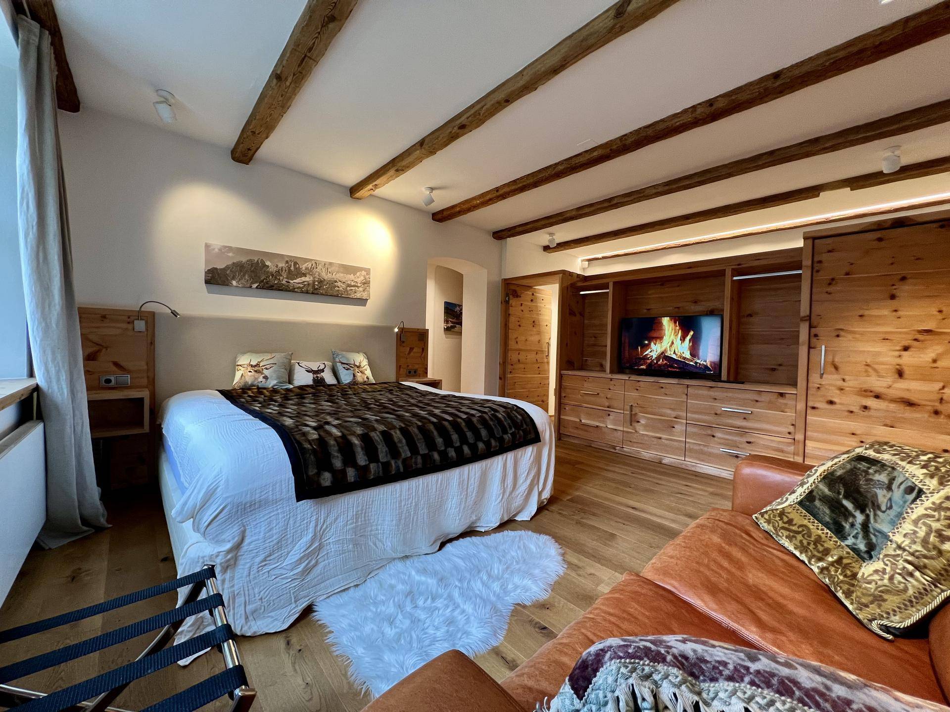 Gemütliches Schlafzimmer mit Holzbalken, Parkettboden und einem großen Bett mit dekorativen Kissen.