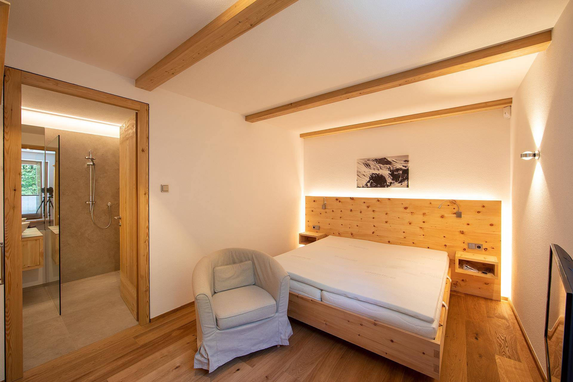 Komfortables Schlafzimmer mit Holzbett, indirekter Beleuchtung und Zugang zu einem modernen Bad.