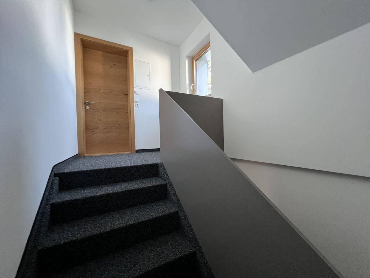 Treppenhaus mit dunklem Teppichboden und Holzdetails, führt zu den oberen Etagen.