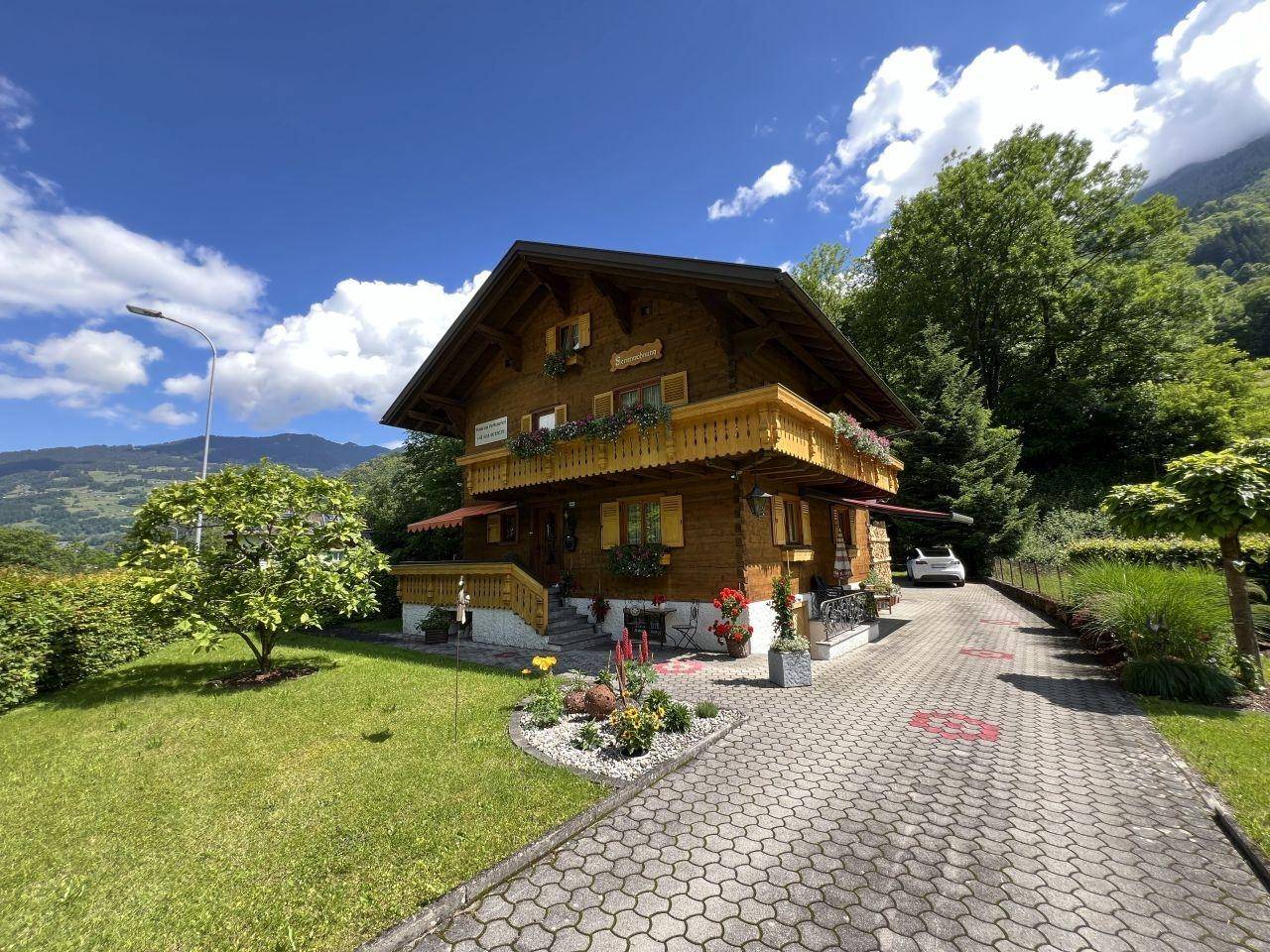 Charmantes Holzhaus im alpinen Stil mit gepflasterter Auffahrt und umgebender Natur.