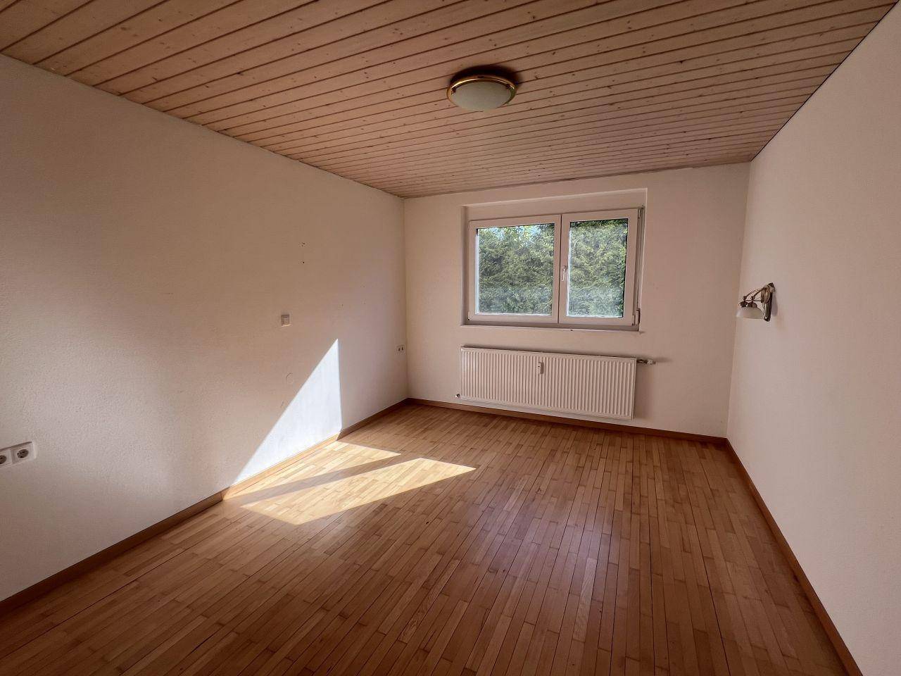 Gemütliches Schlafzimmer mit Parkettboden, Holzdecke und einem Fenster mit grüner Aussicht.