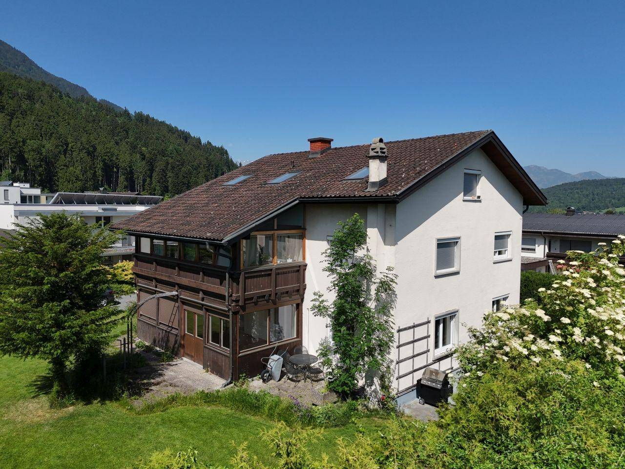 Rückansicht des Hauses mit Gartenbereich, Sitzgelegenheit und Blick auf die bewaldeten Berge.