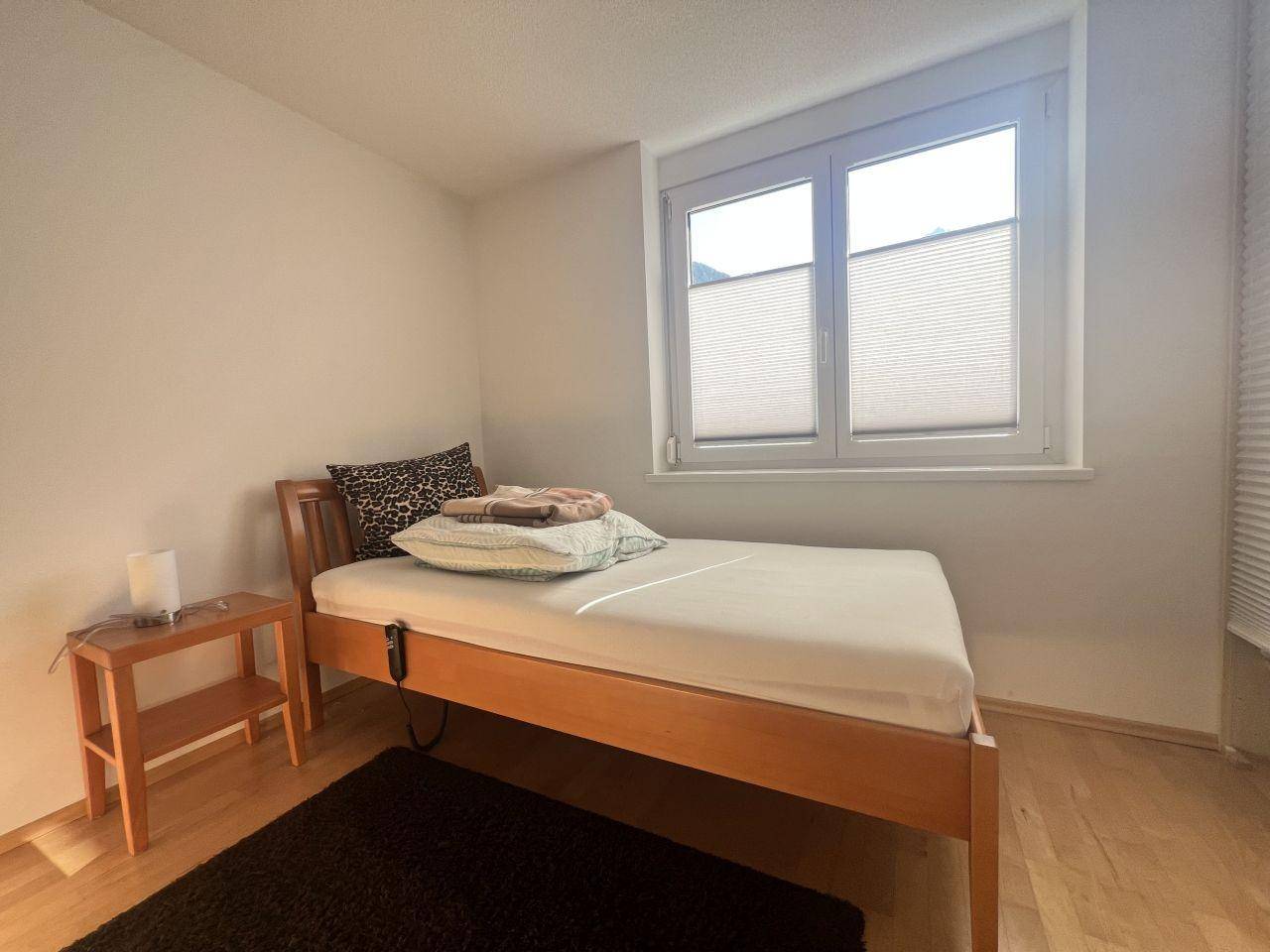 Gemütliches Schlafzimmer mit Einzelbett, Holzboden und Fenster mit Plissees.