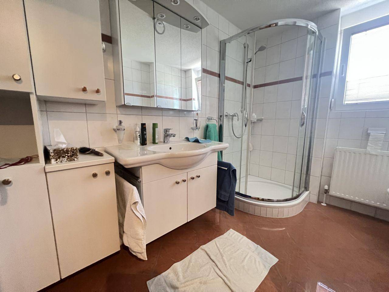 Badezimmer mit Eckdusche, Einzelwaschbecken, Spiegelschrank und Fenster.