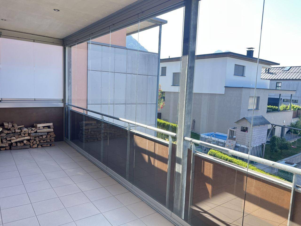 Geräumige Loggia mit gestapeltem Brennholz und Blick auf benachbarte Gebäude und einen Pool.
