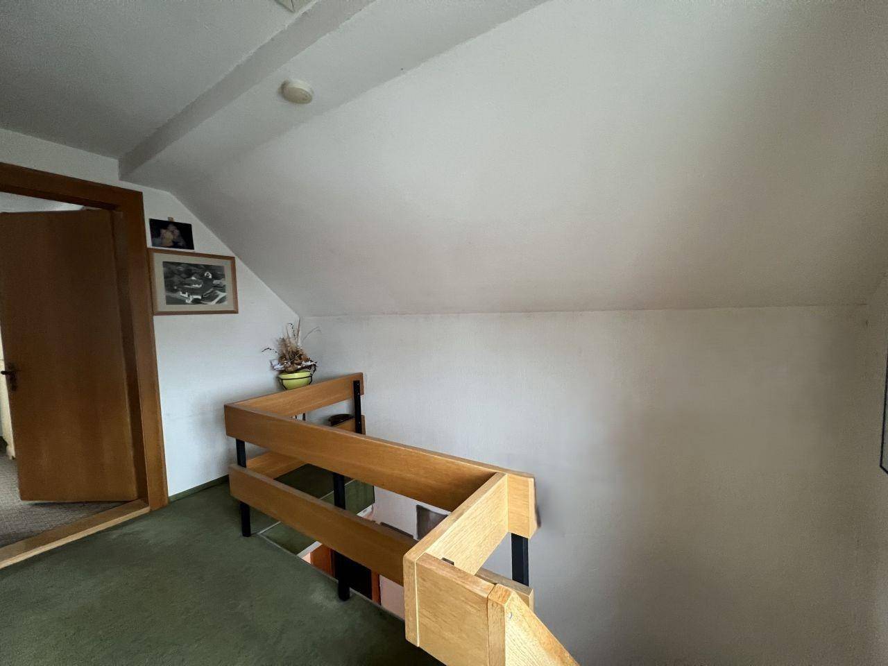 Flur mit Holzgeländer, grünem Teppichboden und Dachschräge im Obergeschoss.