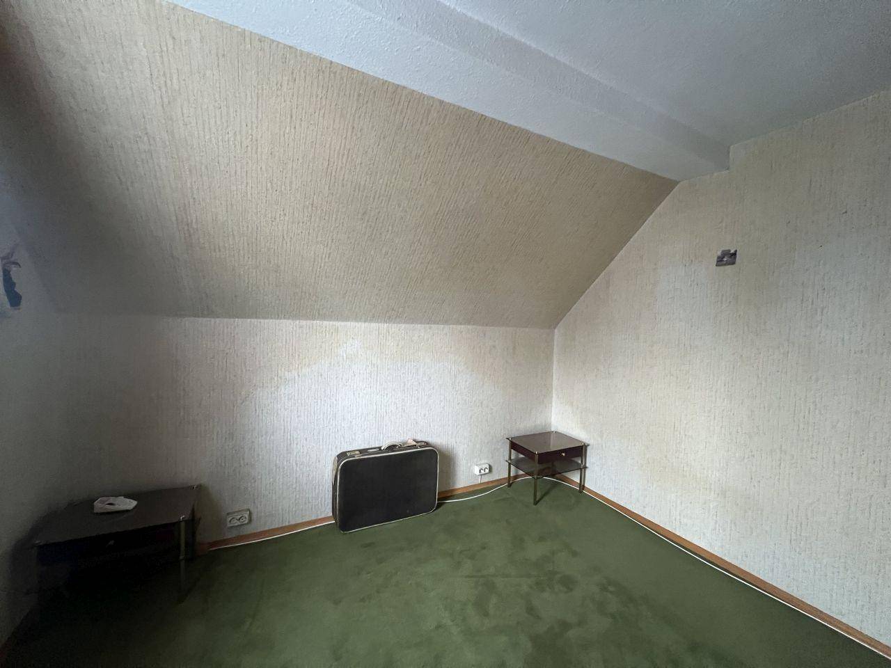 Leeres Zimmer mit Dachschräge und grünem Teppichboden, ideal als Kinderzimmer.