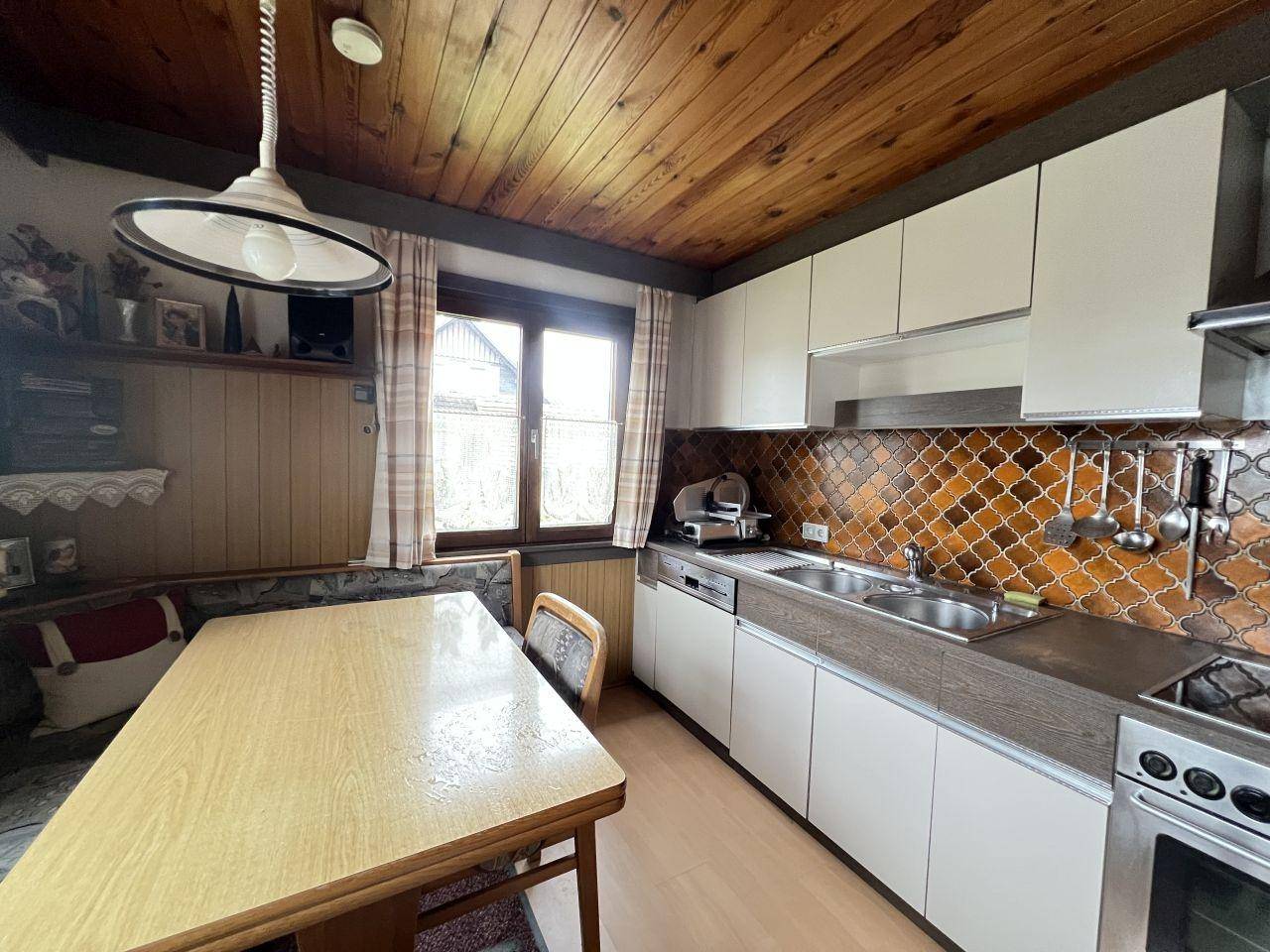 Gemütliche Wohnküche mit Holzbalkendecke, Essbereich und traditionellen Fliesen.