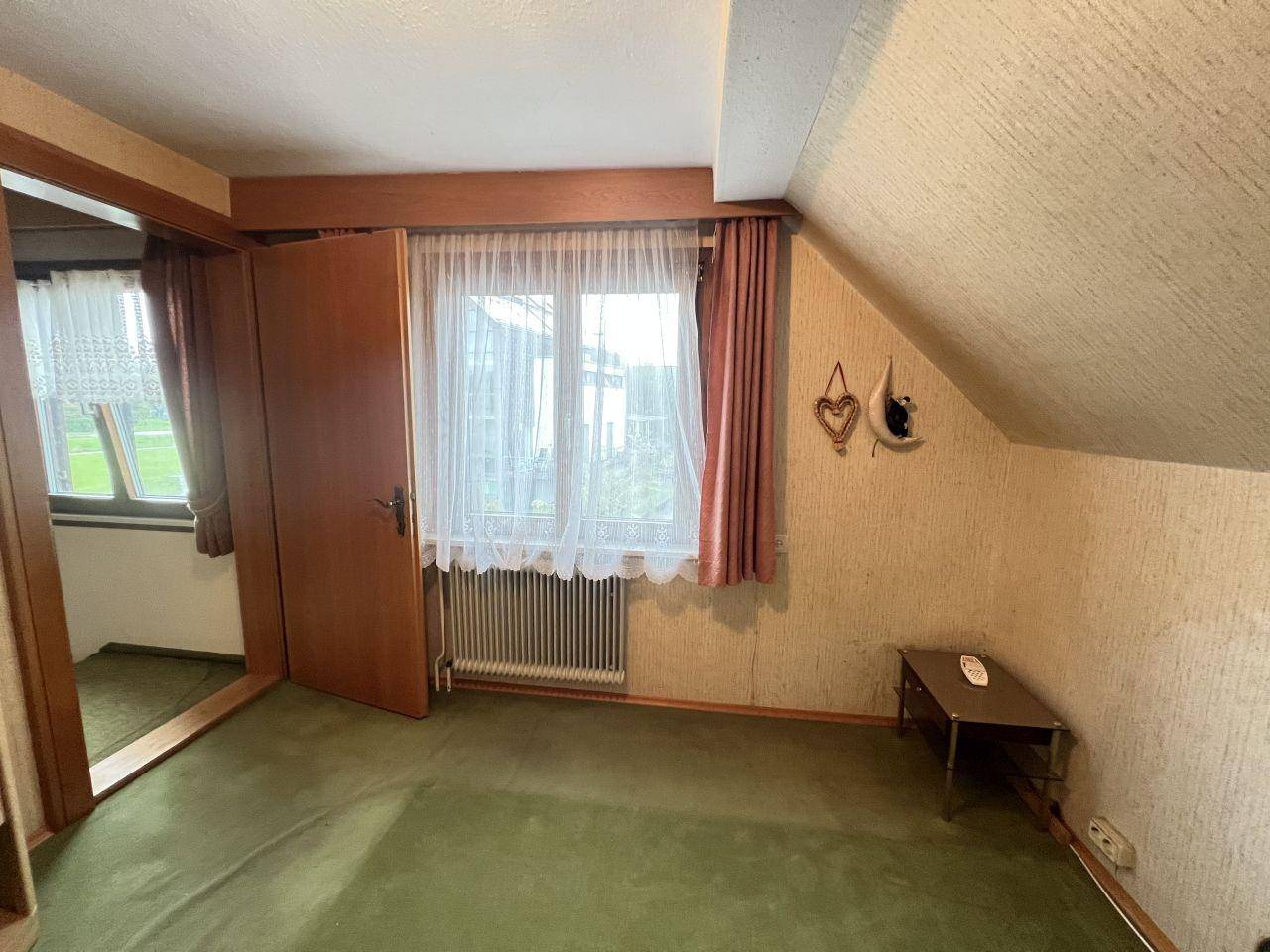 Weiteres Schlafzimmer mit grünem Teppichboden, Dachschräge und Fenster.