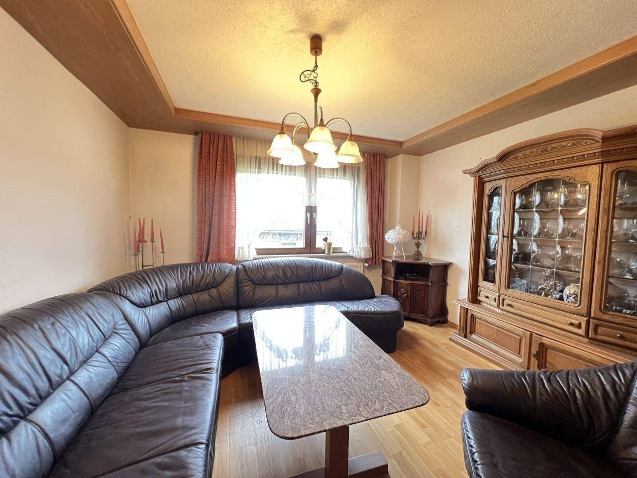 Geräumiges Wohnzimmer mit Ledersofa, Holzmöbeln und Blick nach draußen.