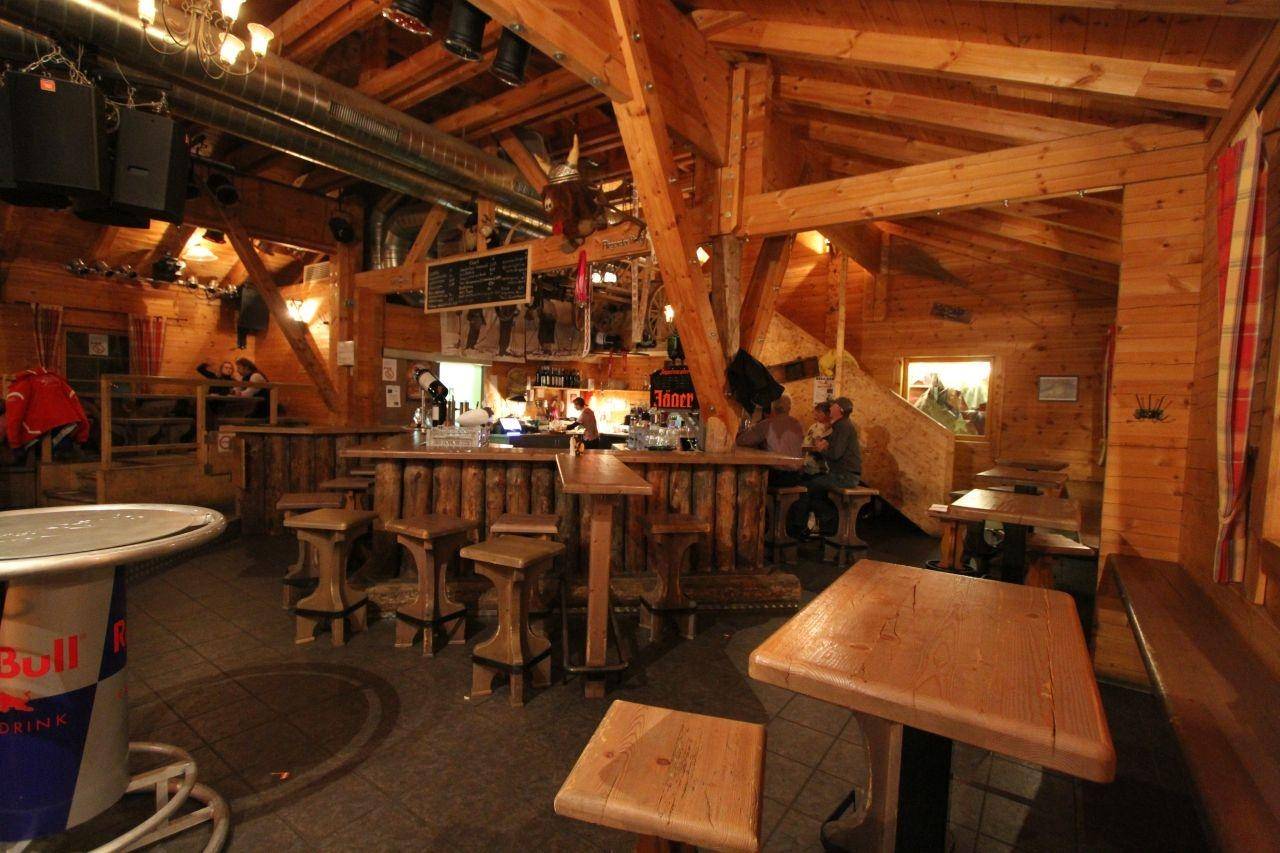 Gemütlicher Barbereich mit rustikaler Holztheke, passenden Hockern und Tischen, umgeben von warmen Holzvertäfelungen.