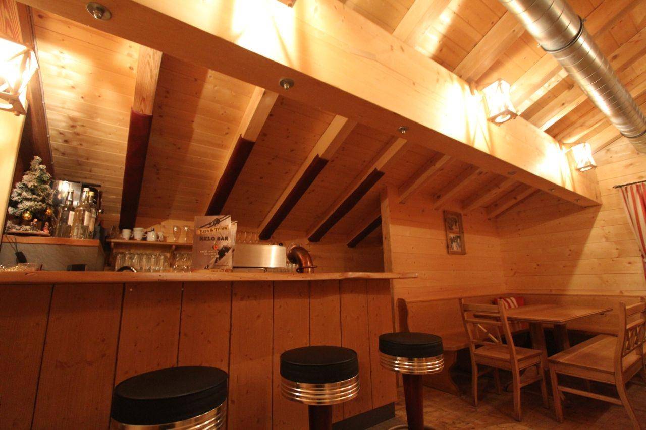 Heller Barbereich mit Holztheke und Sitzgelegenheiten, ergänzt durch Holzwände und sichtbare Deckenbalken.