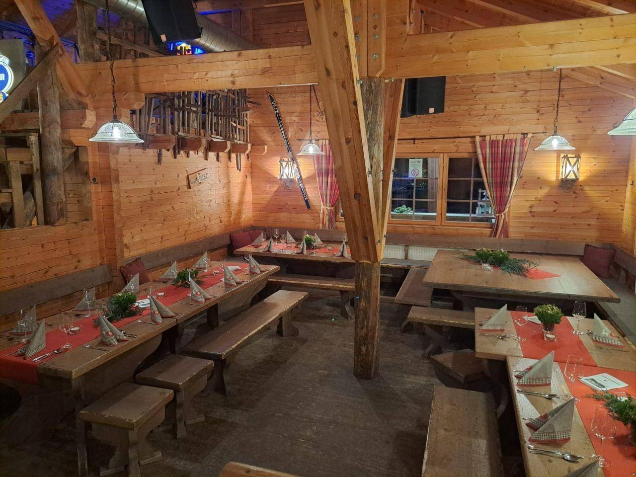 Rustikaler Essbereich mit Holztischen und Bänken, festlich gedeckt, umgeben von warmen Holzvertäfelungen und sichtbaren Balken.