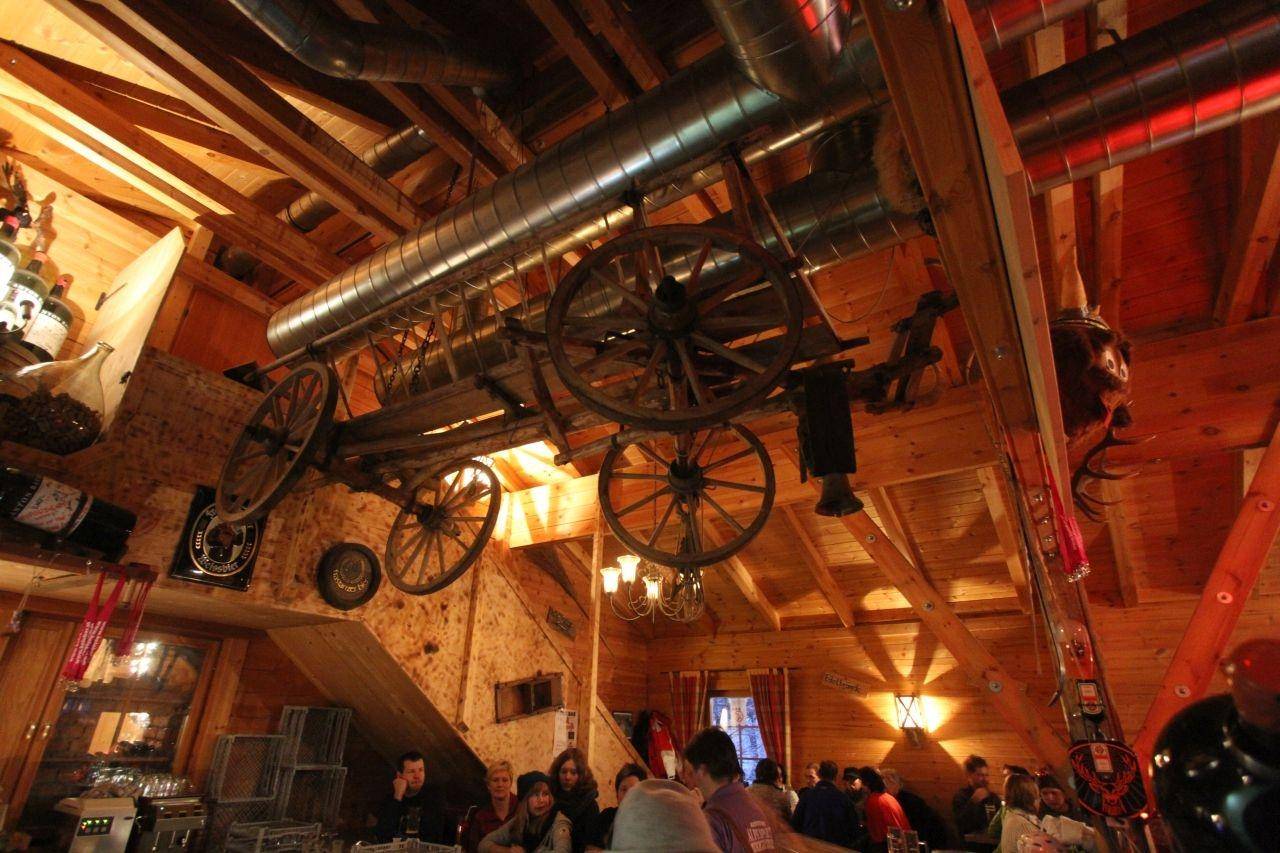 Innenansicht eines Restaurants mit hohen Holzdecken, sichtbaren Lüftungsrohren und dekorativen Wagenrädern als Akzente.
