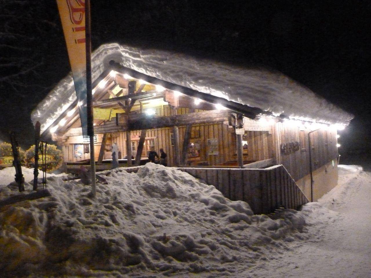 Verschneites Holzgebäude bei Nacht, beleuchtet von warmen Lichtern, eingebettet in eine winterliche Landschaft.