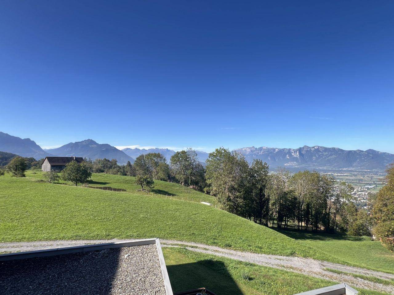 Weitläufiger Blick über grüne Hügel und die majestätische Bergkette unter blauem Himmel.