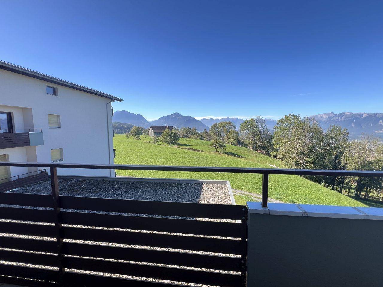Balkon mit Panoramablick auf die umliegende Berglandschaft und weite grüne Wiesen.