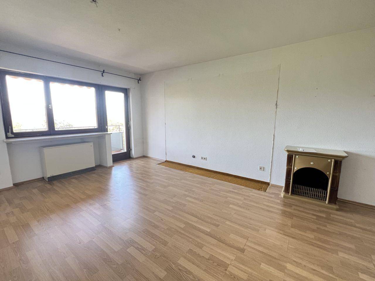 Helles Wohnzimmer mit Laminatboden, großem Fenster und Zugang zu einem Balkon.