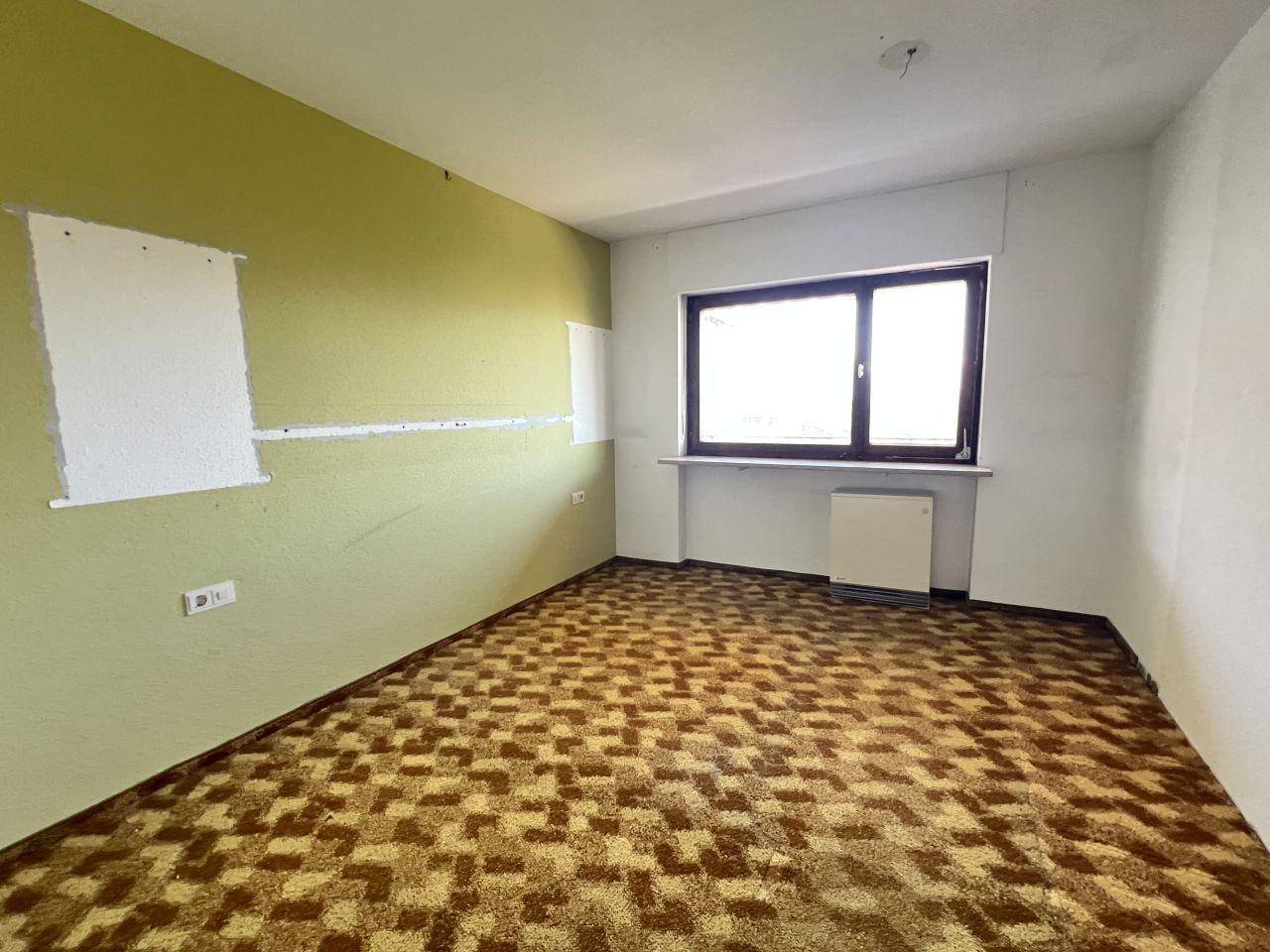 Schlafzimmer mit gemustertem Teppichboden, hellem Fenster und teilweise grünen Wänden.