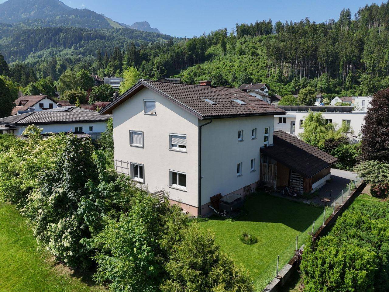 Rückansicht des Hauses mit gepflegtem Garten und bewaldeten Hügeln im Hintergrund.