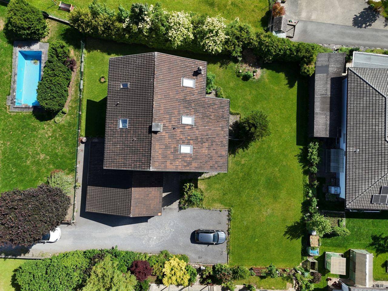 Luftaufnahme des Grundstücks mit Einfamilienhaus, Garten, Pool und Parkplatz.