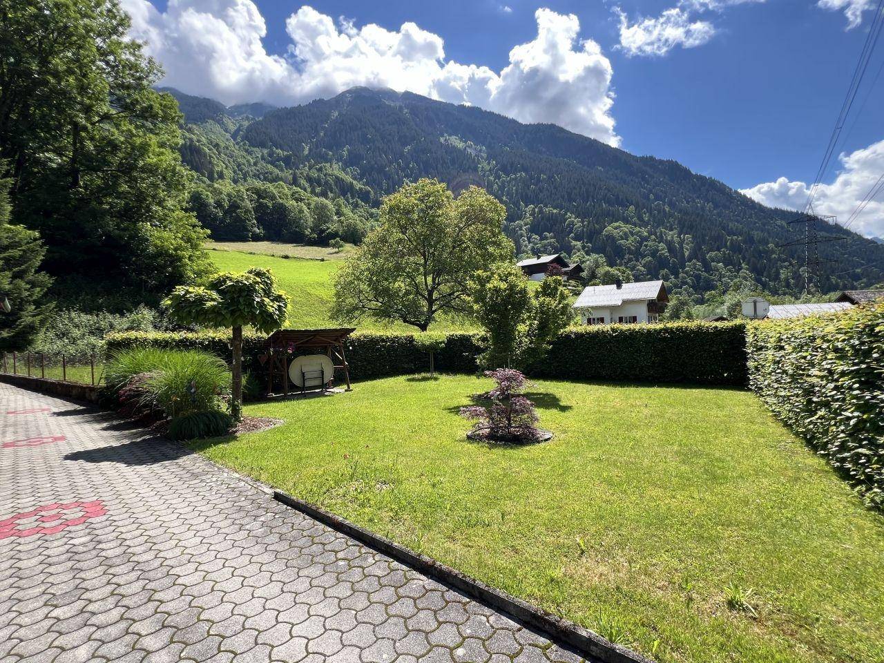 Gepflegter Rasenbereich mit Hecken und Bäumen, umgeben von einer malerischen Berglandschaft.