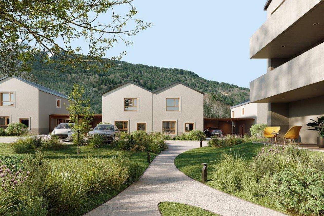Moderne Wohngebäude in einer grünen Umgebung mit gepflegten Gärten und Bergblick.