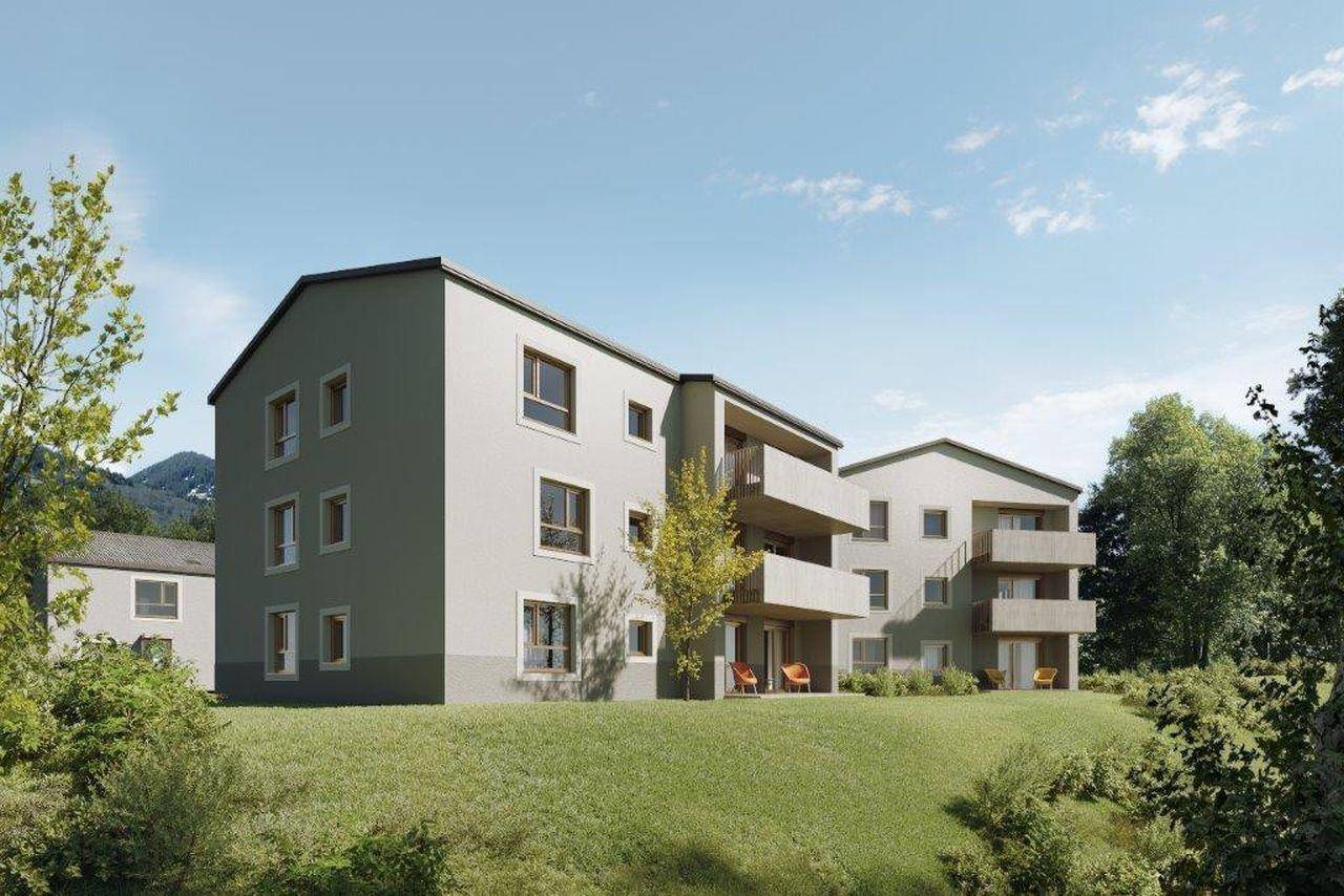 Mehrere moderne Wohngebäude eingebettet in eine grüne Landschaft mit Bäumen und Rasenflächen.