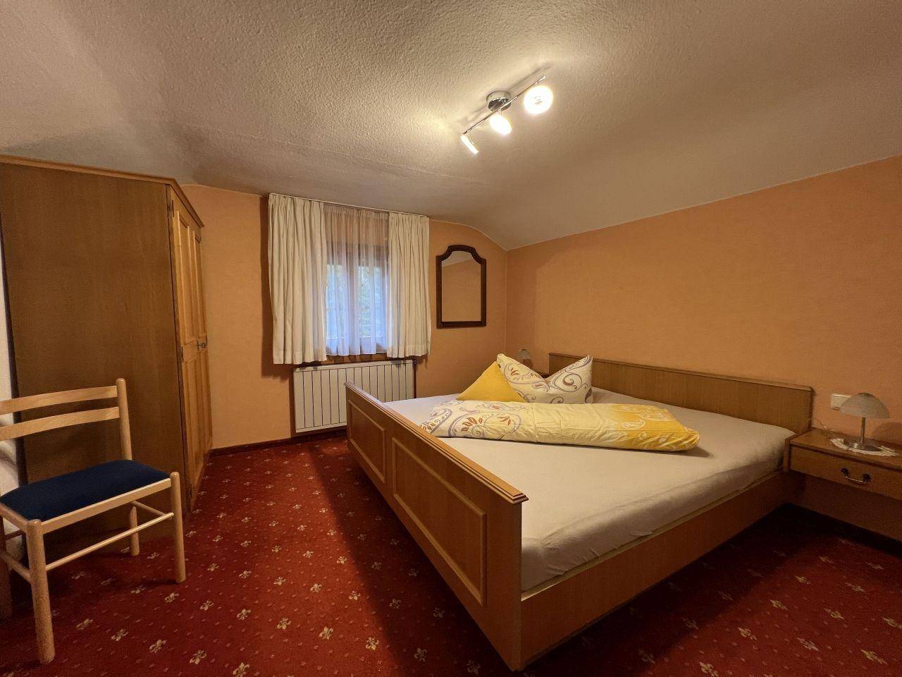 Geräumiges Schlafzimmer mit Doppelbett, rotem Teppichboden und Holzschrank.