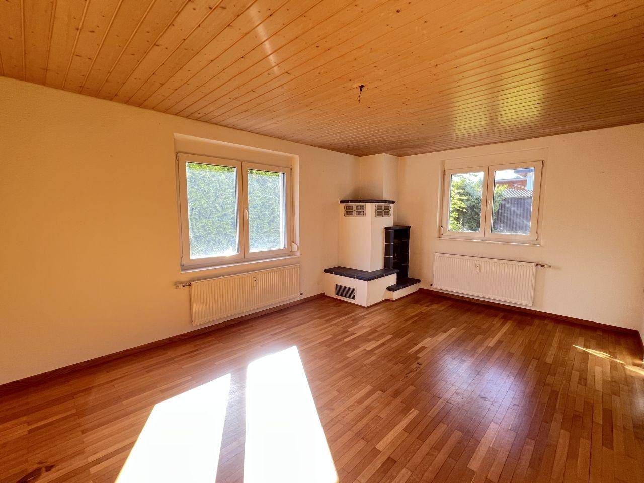 Heller Wohnraum mit Holzparkett, Holzdecke und einem traditionellen Kachelofen.