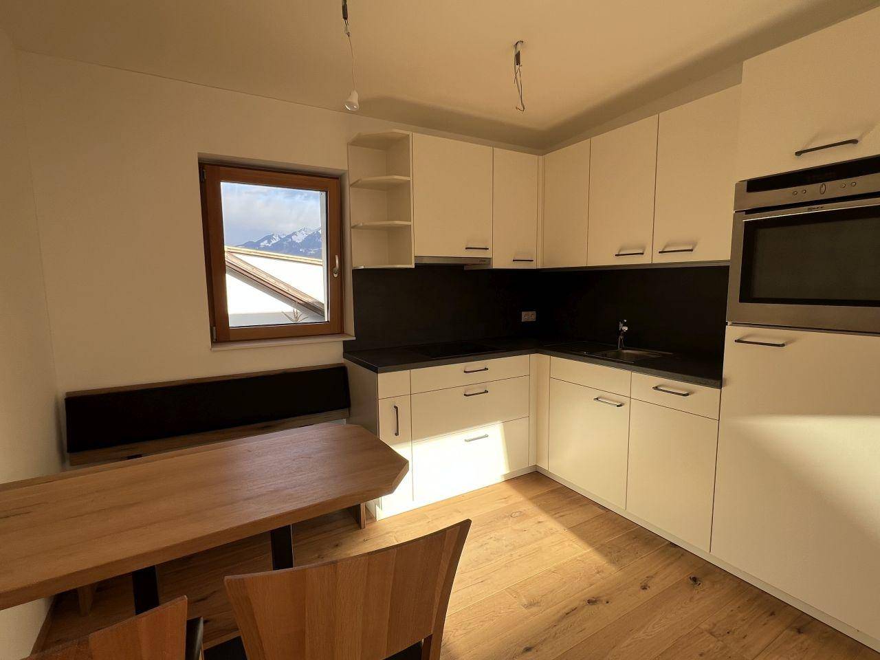 Helle Einbauküche mit weißen Schränken, Holzboden und Essbereich, mit Bergblick durch das Fenster.