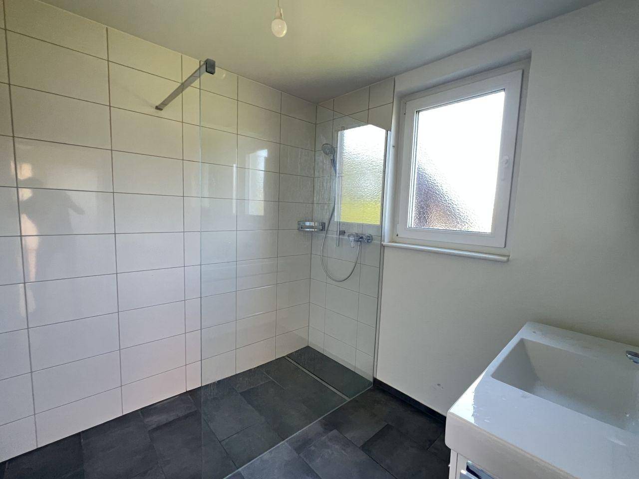 Modernes Badezimmer mit ebenerdiger Dusche, weißen Fliesen und einem Fenster für Tageslicht.