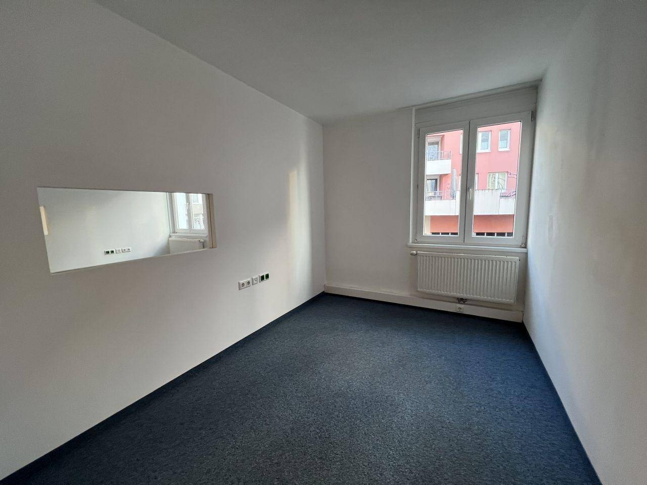 Geräumiges Zimmer mit blauem Teppichboden und viel Tageslicht durch die Fenster.