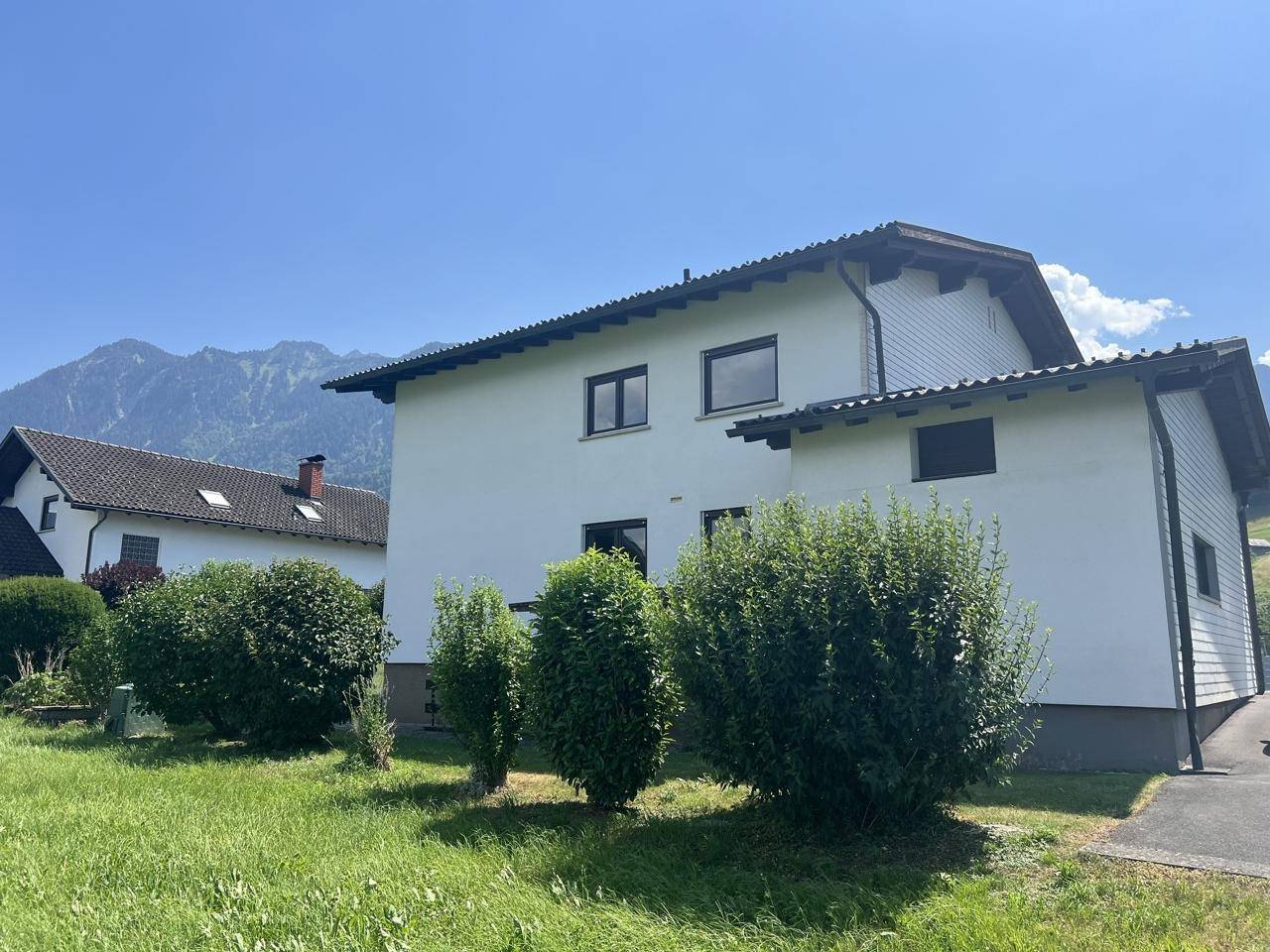Seitenansicht des Hauses mit gepflegten Büschen und Blick auf die Berglandschaft.