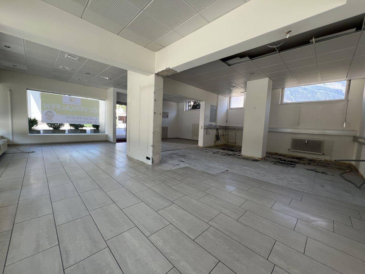 Großer, leerer Geschäftsraum mit Fliesenboden, abgehängter Decke und sichtbaren Installationsvorbereitungen.